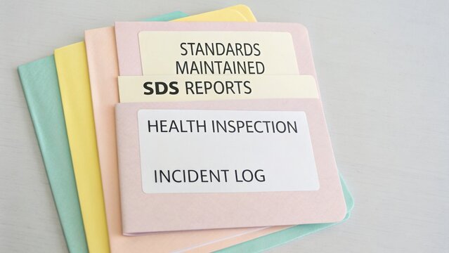 Organized file folders with health inspection reports, safety data sheets, and incident logs for effective documentation management