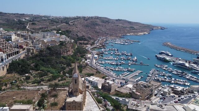 Drone view of Mgarr harbour in Gozo Island, Malta. Church of the Madonna of Lourdes in the foreground . High quality 4k footage