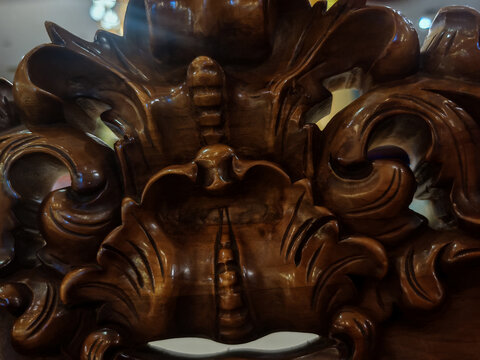 an intricately carved wooden mask sculpture featuring detailed ornamental craftsmanship and symmetrical facial design. The image highlights texture, material depth, and traditional decorative artistry