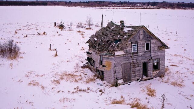 Cinematic drone shot panning past a rustic, run-down barn surrounded by winter scenery.