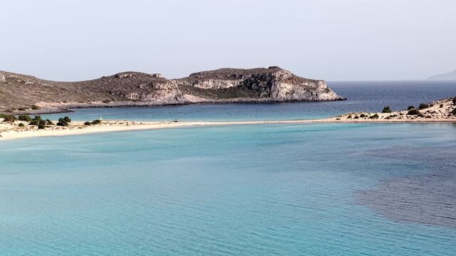 Drone shot of Simos beach double bay divided by sandy strip with rugged limestone mountain in background into Aegean Sea, Elafonisos island