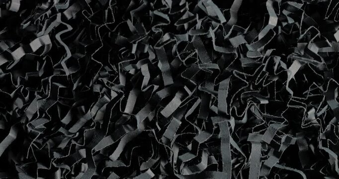Black shredded paper. Close-up of dense black cut and crumpled paper strips forming chaotic layered texture. Smooth continuous rotation reveals dynamic shifts in light and deep shadows.