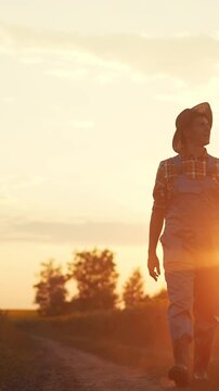 A man walks along a dirt path during sunset. The man is wearing work attire while the sun sets behind trees, creating a warm glow in the landscape.