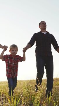 A man and a boy stand together in a field. The man holds the boy's hand as they look towards the horizon in the open, grassy landscape.