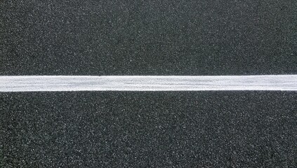 Fototapeta premium A stark white line divides a textured dark gray asphalt surface