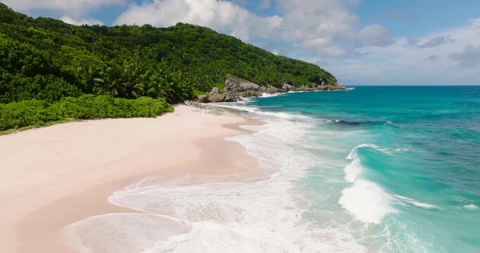Clear turquoise water approaching a sandy beach with lush green foliage in the background. Seychelles, Mahe. Petit Boileau.