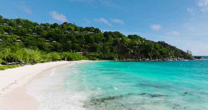 Pristine white sandy beach with turquoise waves, surrounded by dense tropical greenery. Seychelles, Mahe.