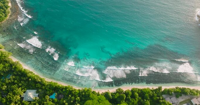 Crystal clear turquoise waters rolling onto a sandy tropical beach surrounded by lush greenery. Seychelles, Mahe.