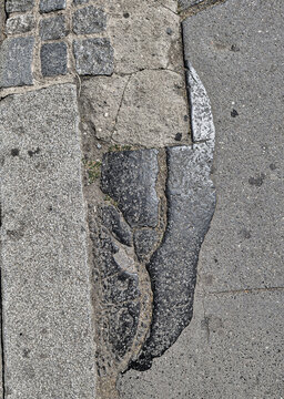 Cracked asphalt patch on concrete sidewalk, weathered urban pavement texture with damaged infrastructure