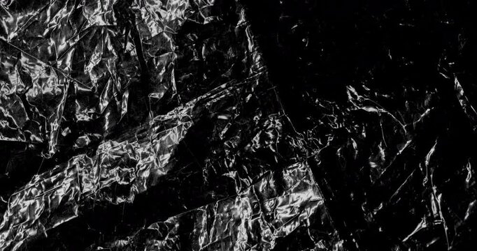 Crumpled black metallic foil. Close-up reflective black foil with deep folds and highlights, smooth rotation. Ideal for luxury, abstract and industrial backgrounds.  
