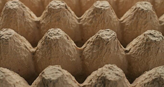 Recycled paper. Close-up of empty beige molded pulp tray with rough fibrous surface and conical cells. Smooth continuous rotation shows subtle light and shadow shifts across the eco recycled texture.	