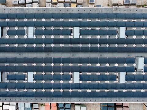 Aerial view of a paving stone factory roof featuring extensive solar panel arrays and stacks of paving materials in the yard below in Riga, Latvia.