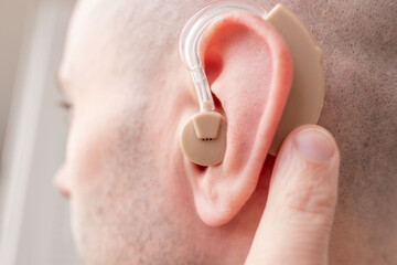 Fototapeta premium Young man with beige hearing aid in ear, close up portrait, BTE hearing support, accessibility, modern technology, inclusion, health care, confidence and everyday life, Modern healthcare solutions