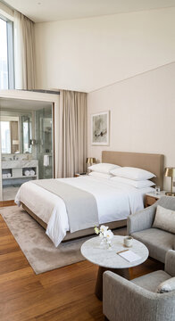 Professional housekeeping detail featuring a spacious room with made bed, gray runner, sofa, armchair, coffee table, and open bathroom for hotel cleanliness and guest room preparation