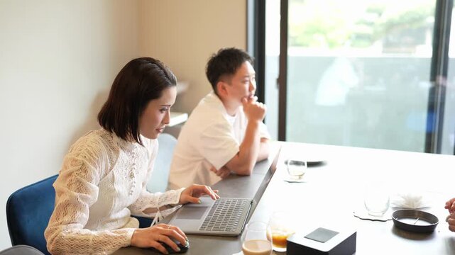 Two colleagues collaborate at a modern desk. Woman types intently, man observes thoughtfully. Natural light fills the bright office space. Ideal for business, teamwork, or remote work concepts