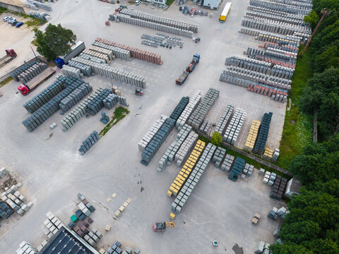 Aerial view of a paving stone factory with organized stacks of concrete pavers, trucks, and forklifts in an industrial yard in Riga, Latvia.
