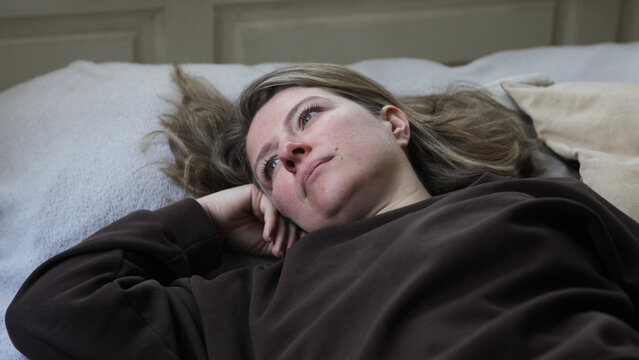 Middle aged woman lying on a bed in an emotionally withdrawn pose with a depressed expression. Concept of depression, mental health, loneliness, emotional distress, burnout, anxiety,.