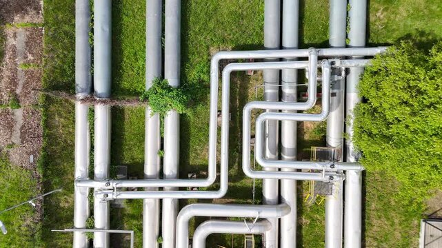 Aerial view of interconnected industrial pipes with green grass and walkways visible, showcasing the complex layout of a facility's piping system in an industrial setting