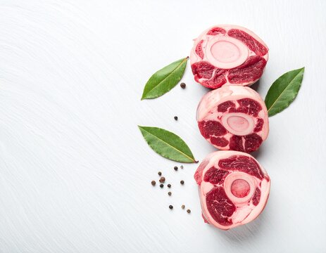 Thick slices of raw beef oxtail with bay leaves on a white slate surface.