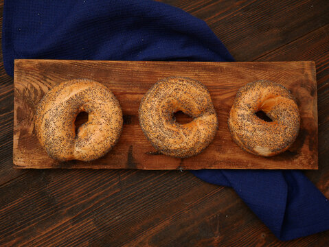 Three plain bagels are arranged in a row on a wooden board, with a dark blue cloth draped behind them.