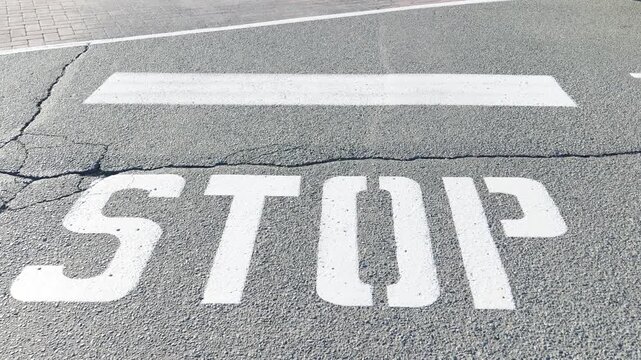 Painted white stop sign and limit line on cracked asphalt road
