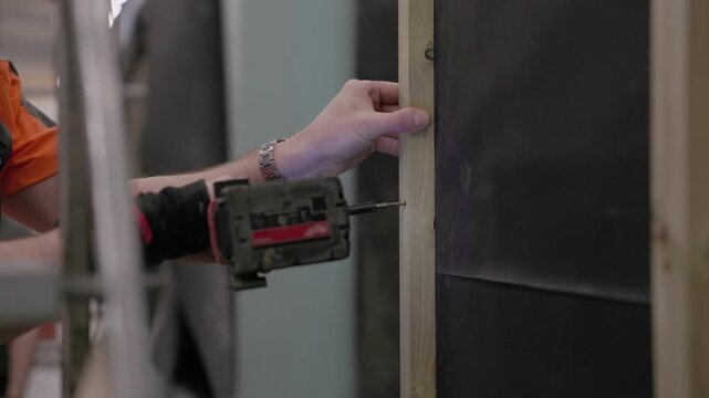 Worker using cordless drill to screw a wood stud into wall framing during interior home construction