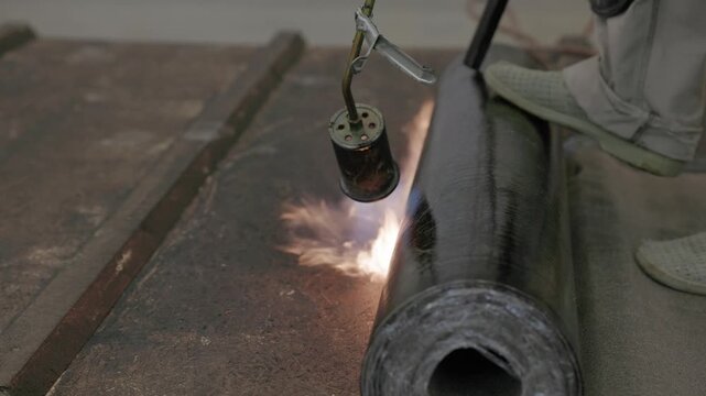 Close-up of flame torch welding modified bitumen roofing membrane on wooden decking during waterproofing installation