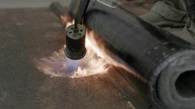 Close-up of flame torch welding modified bitumen roofing membrane on wooden decking during waterproofing installation