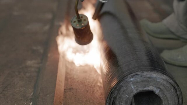 Close-up of flame torch welding modified bitumen roofing membrane on wooden decking during waterproofing installation