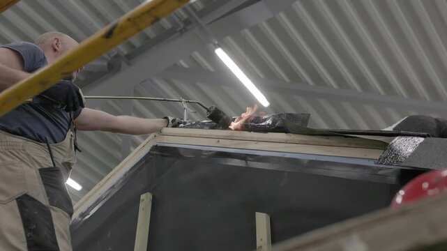 Close-up of flame torch welding modified bitumen roofing membrane on wooden decking during waterproofing installation