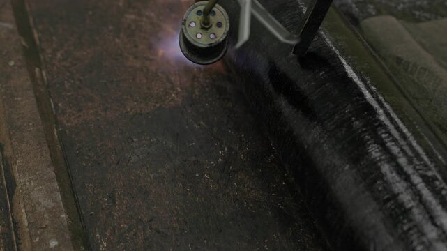 Close-up of flame torch welding modified bitumen roofing membrane on wooden decking during waterproofing installation