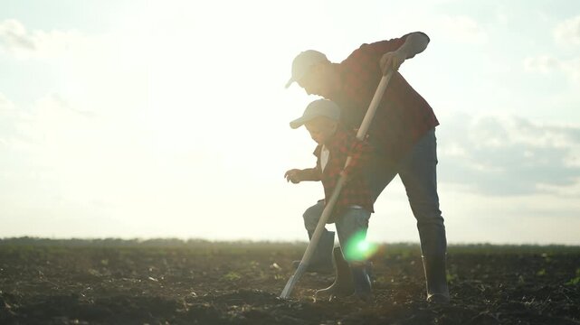 Father teaches son to farm. Agriculture concept as father shows son how to use shovel in field. Father and son bonding over agriculture. Rural farming education. Father guiding son in agriculture work