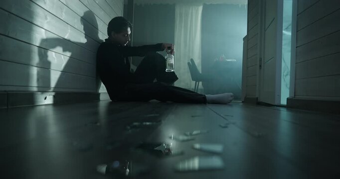 Depressed drunk man sit floor dark room drink alcohol bottle. Sad male suffer alco addiction, loneliness. Social problem, crisis, mental health struggle concept. Alcoholic guy feel grief, anxiety doom