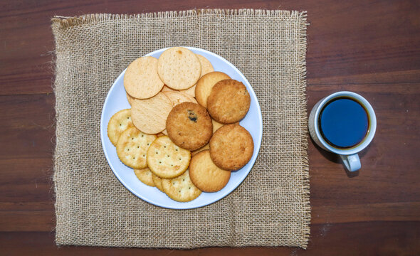 Assorted cookies and biscuits on a plate with black coffee on a wooden table. A collection of sweet baked snacks including chocolate cookies, butter biscuits, crackers