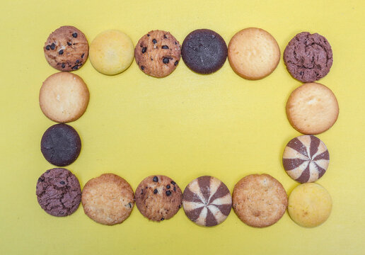 Assorted cookies and biscuits arranged in a square shape copyspace isolated on yellow background. Collection of sweet baked snacks including chocolate cookies