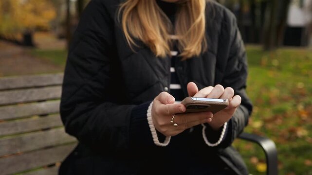 Close up view of a caucasian female hands typing on mobile phone screen against blurry green nature background.