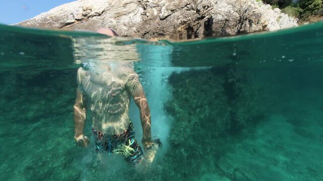 Boy jumping into sea water split shot over under half underwater view