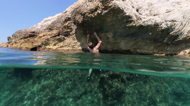 Boy climbing rock split shot over under half underwater