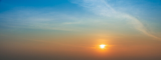 Fototapeta premium Golden sunset glowing beneath a blue sky with soft clouds and warm evening light.