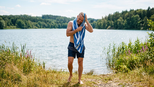middle aged man drying off with towel after swimming in bathing lake at local recreation area