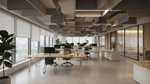 Office desks stand in a modern workspace featuring acoustic ceiling baffles and large windows overlooking the city.