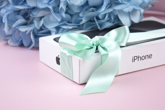The box with an iPhone 15 Pro Max phone with a bow as a gift on a pink background.