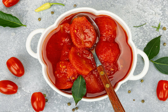 Canned whole peeled tomatoes in tomato juice in a white ceramic bowl with spoon. Rustic food styling