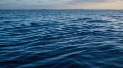 Naklejka premium Deep blue ocean water with gentle ripples on the surface. Soft evening sky on the horizon in the background.