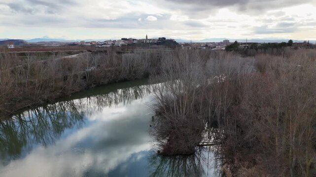 Aerial descending view of Haro town skyline from Ebro river with sky reflections on water