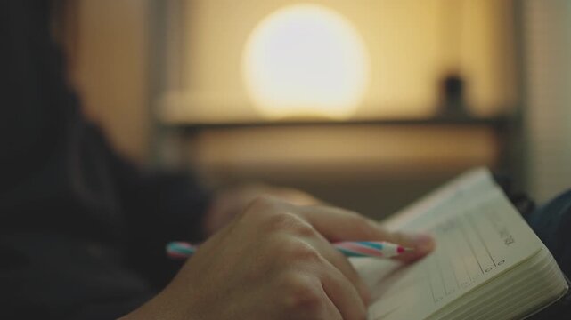 Close-up of Hand Holding Pen and Touching Diary Notebook While Thinking and Planning at Night.