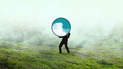 Naklejka premium Businessman carrying round sky mirror in misty green landscape. Concept of clear vision, future planning, creative leadership, sustainability strategy, fresh perspective.