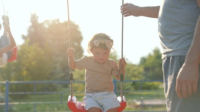 Happy Father pushing daughter on swing in playground. Happy daughter on swing enjoying time with father outdoors. Bonding moment between father daughter. Joyful daughter swinging high in playground.