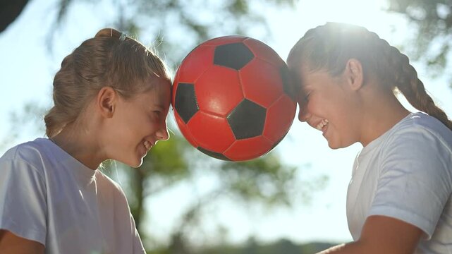 smiling children playing with ball outdoors. children pressing soccer ball between heads. Fun and playful moment outdoors. Children enjoying ball game. Active children lifestyle playing ball outdoors.