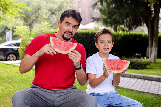 Father and son holding fresh watermelon slices in a sunny park. Happy family lifestyle, healthy summer snack, outdoor recreation, parenting, and childhood memories concept
